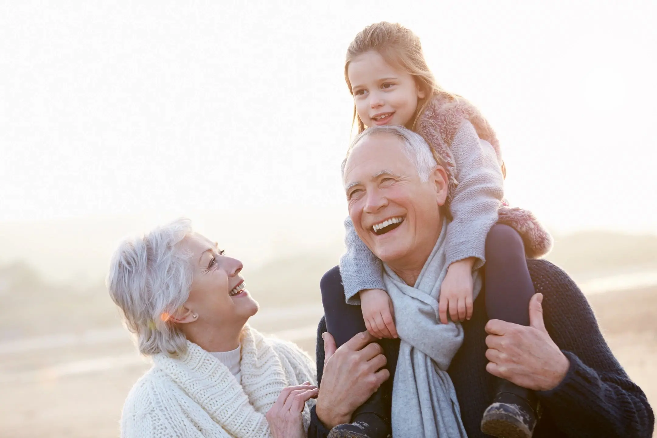 Happy elderly couple with a young girl on the man's shoulders outdoors.