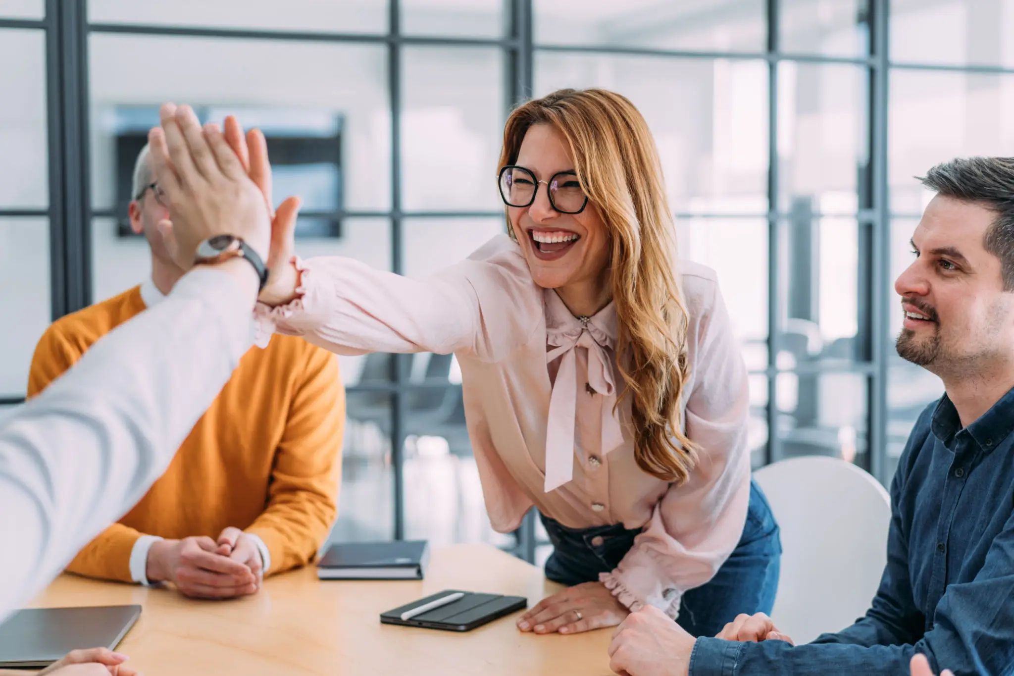 Colleagues sharing a high-five during a meeting in a modern office.