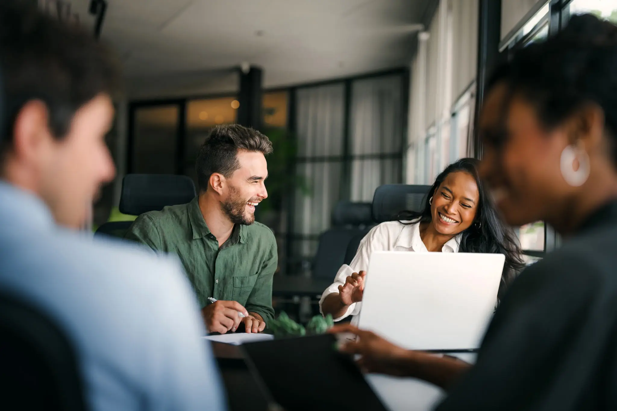 Colleagues collaborating and smiling during a meeting with a laptop.